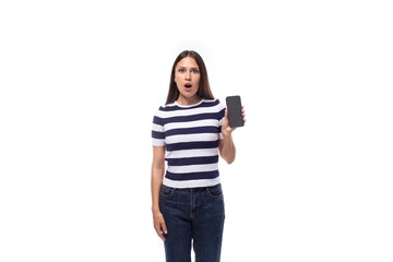 young surprised brunette european lady of slim build dressed in a striped summer t-shirt holding a smartphone screen forward with a mockup