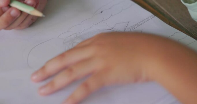 Asian child with black hair with a smiling face lying on the floor of his house drawing picture of a girl with braids. using his imagination creating art. Concept of children, learning, creativity. 4k