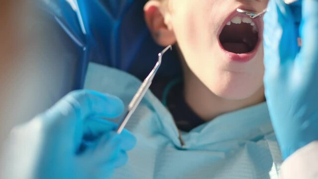 Caring female dentist using dental probe and angled mirror while doing tooth decay status on a young patient

