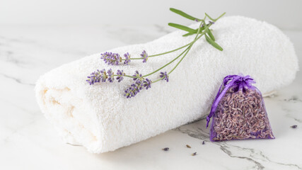 Purple lavender flowers on white soft towel with aroma sachet on marble table background.