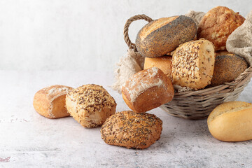 Fresh crispy bread buns in basket on grunge stone table background. Poppy, sesame, flax and...