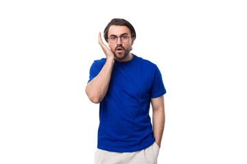 young shocked european brunette man with beard dressed in blue t-shirt on studio background