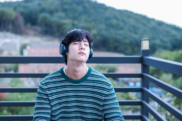 A young college student who enjoys relaxing and contemplating while listening to music on his headphone in the green natural space