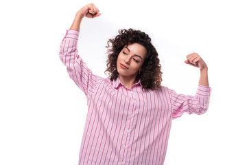 young cute curly-haired caucasian woman dressed in a striped pink blouse actively gesticulates with...