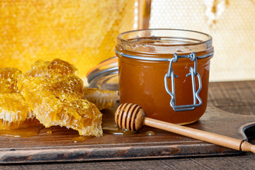 A glass jar of thick golden honey with wooden spoon and honeycombs. Concept of beekeeping,...