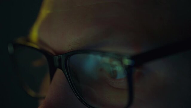 A monitor flickering in a dark office is reflected in the glasses of a programmer engrossed in late-night development. Using advanced technologies, program codes are created on a portable laptop