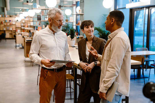 Group of diverse colleagues discussing business issues while standing in modern co-working space
