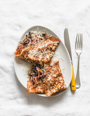 Crepes stuffed with fried mushrooms, ham and cheese on a light background, top view