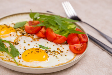 Fried eggs with tomatoes and arugula on a plate.
