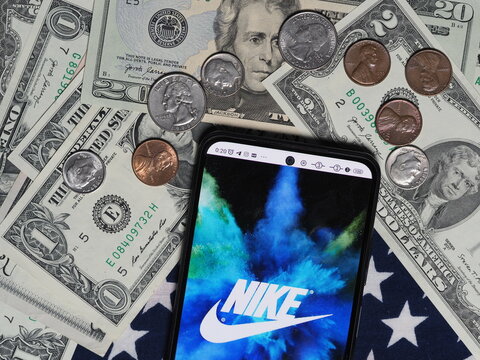 In this photo illustration, a Nike, Inc. corporation logo seen displayed on a smartphone with United States Dollar notes and coins in the background.