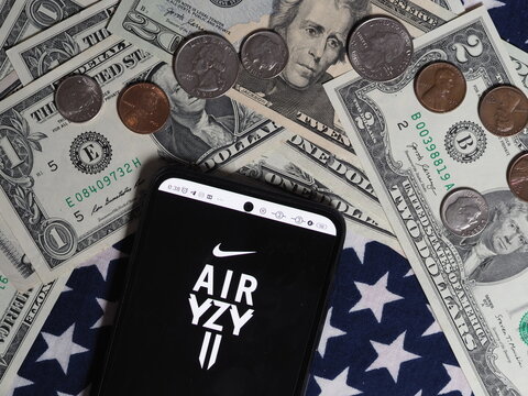 In this photo illustration, a Nike Air Yeezy logo seen displayed on a smartphone with United States Dollar notes and coins in the background. Nike Air Yeezy brand owned by Nike, Inc. corporation