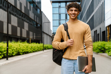 Young business man smiling at camera while standing outdoors near office buildings