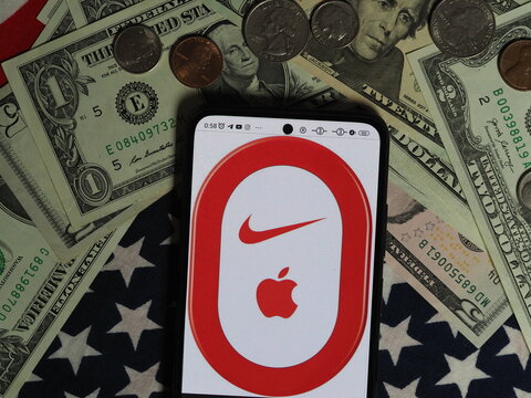 In this photo illustration, a Nike+iPod logo seen displayed on a smartphone with United States Dollar notes and coins in the background. Nike+iPod brand owned by Nike, Inc. corporation
