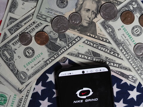 In this photo illustration, a Nike Grind logo seen displayed on a smartphone with United States Dollar notes and coins in the background. Nike Grind brand owned by Nike, Inc. corporation