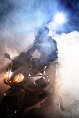 Motorcyclist in a leather jacket suit through the red and blue smoke on a motorcycle at night