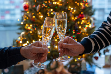 New year or christmas dinner, two man hands with glasses of champagne cava or prosecco wine crystal glasses with christmas tree and garland lights on background