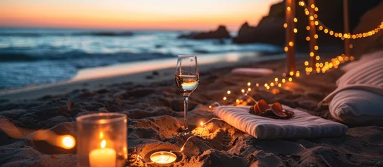 Fototapeten Romantic beach date by California ocean waves with candlelight, wineglass on sand, and cozy lounge garland at sunset. © AkuAku