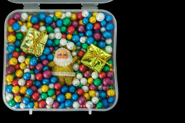 Santa Claus with pile of small colorful thermocol balls and gift box in plastic box isolated on black background.