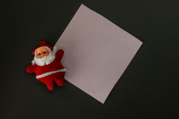 Santa Claus with white sheet of paper on a black background, copy space