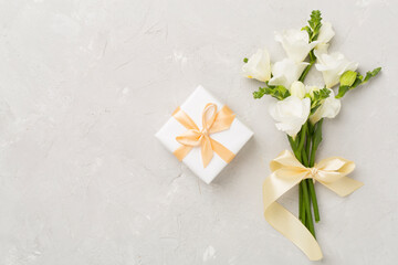 Gift box with fresia flower concrete background, top view