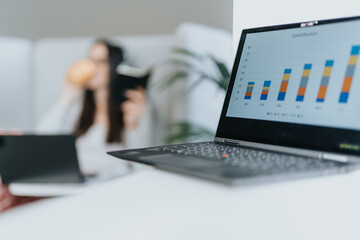 Blurred photo of woman taking a sip from her coffee, focus on lap top with graph charts on the...