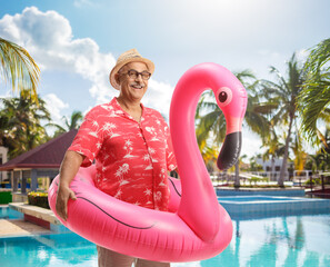 Mature tourist with a big inflatable flamingo rubber ring standing by a swimming pool