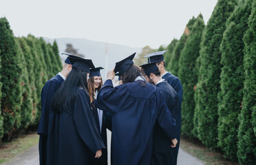 Multiethnic university graduates celebrating their achievement in a park, wearing graduation caps...