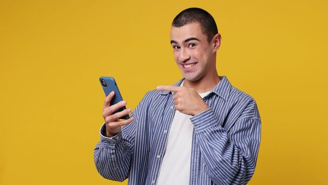 Young middle eastern man he wear blue shirt white t-shirt hold use mobile cell phone typing browsing swipe send sms do online shopping order delivery home book tour isolated on plain yellow background