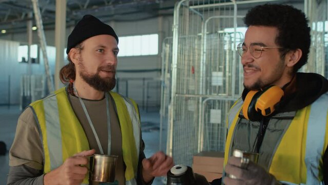 Chest up side shot of smiling diverse colleagues drinking tea and talking during break at warehouse