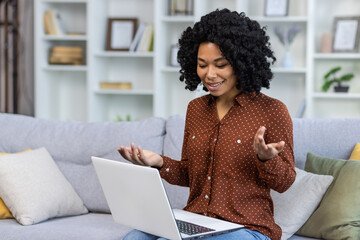 African american young woman talking online video call on laptop sitting on couch at home.