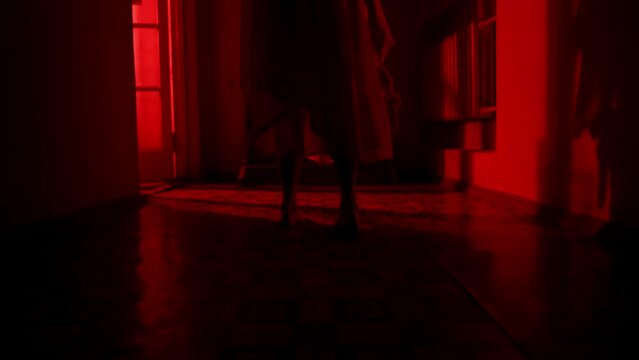 Horror movie and poltergeist creative advertising concept. Female ghost in a house. A woman in a white dress is walking down a hallway holding a toy. Flashing red horror light. Close up.