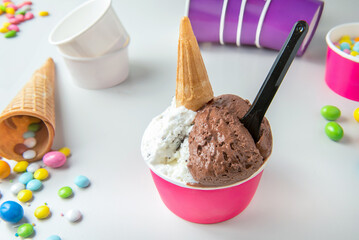 ice-cream with chocolate and stracciatella cream in tub with biscuit cones and sugared almonds on...