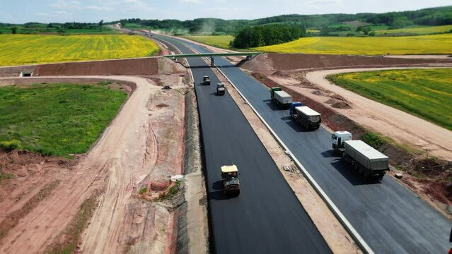 Aerial view of construction equipment building an automobile highway. Heavy equipment, rollers rolling out a new layer of asphalt. 4k footage