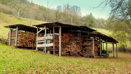 einfacher  Holzschuppen als Holzlager am Berghang in freier Natur mit Wald und grüner Wiese 