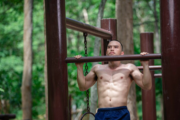 Obraz premium Handsome man exercises by hanging on a bar outdoor, Asian man trains for sporting events