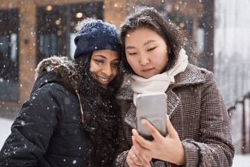 two asian women looking at smartphone screen outdoors in winter city