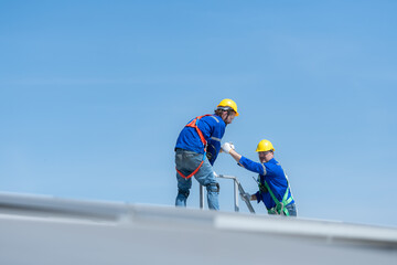 A young technician intern working on solar panels is fear of heights with senior engineers who are...