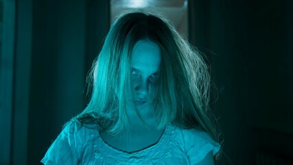 Portrait of ghost female in the house. Woman in white dress with scary face expression looking posing and staring at the camera.