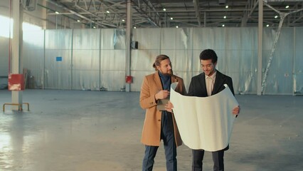 Full medium shot of happy diverse business partners looking at blueprint and inspecting empty spacious building planning new projects