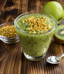 Smoothie with kiwi, green apple and bee pollen in the drinking glass on the wooden background. Close-up.