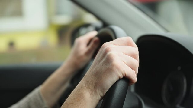 Female driver is driving car along the country road, closeup of hands on vehicle steering wheel, 4K footage