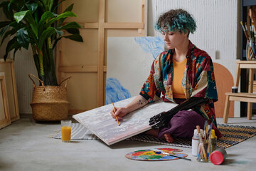Creative teenage girl with prosthetic arm sketching drawing on canvas in studio
