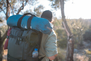 A male tourist with a large backpack and equipment on a mountain trail among the trees.
