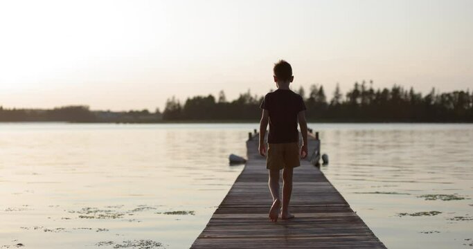 Young boy walking on dock on open ocean looking around nervously