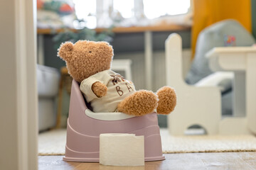 A toy bear sits on a baby potty in a room, the concept of potty training a child