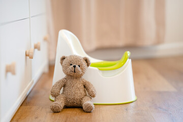 A toy bear sits on a baby potty in a room, the concept of potty training a child - obrazy, fototapety, plakaty