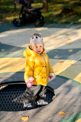 Fototapeta premium A child toddler in a yellow jacket jumps on a trampoline in the playground in autumn