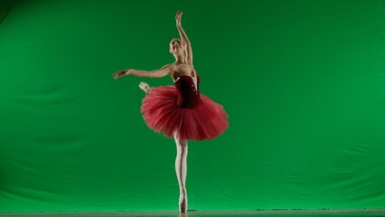 Woman on chroma key background of green screen. Beautiful ballerina in red tutu and pointe shoes dancing on toes choreography in studio. © kinomaster