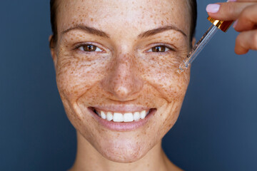 Moisturizing and nourishing skin care serum. Close up beauty portrait of  beautiful woman with a freckles  is applying a vitamin c sincare sebum with a pipette dropper.