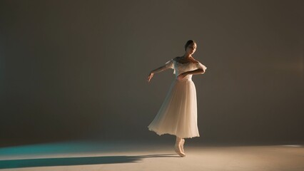 Portrait of female on soft background in warm light in studio. Beautiful ballerina in white tulle...